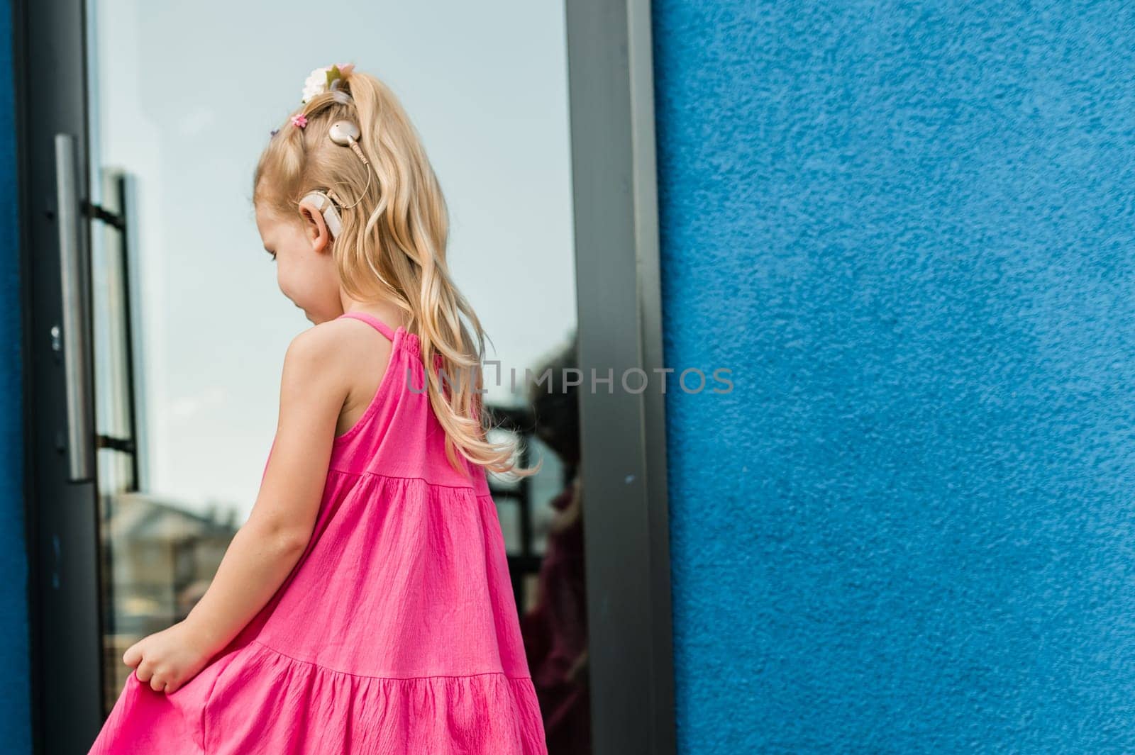 Child girl with hearing aid and cochlear implantation system. Kid with hearing problems walks outdoor in summer. Inclusion and diversity