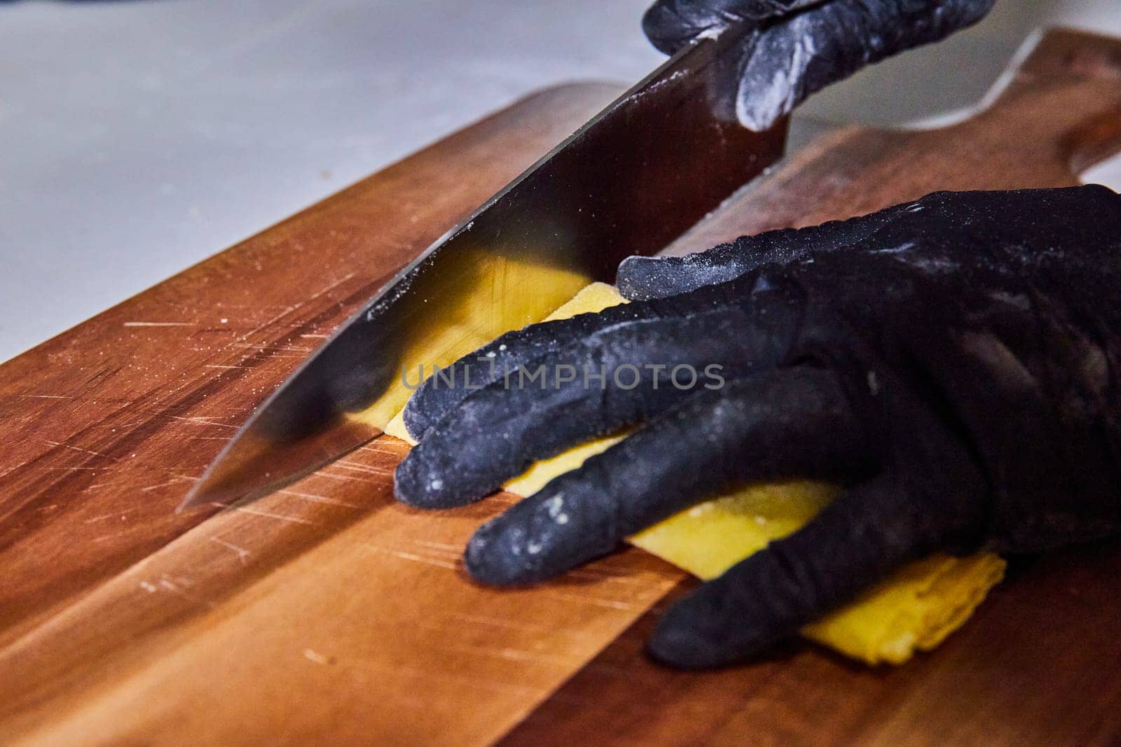 Culinary Precision: Gloved hand slicing homemade pasta on a rustic board in Fort Wayne, Indiana.