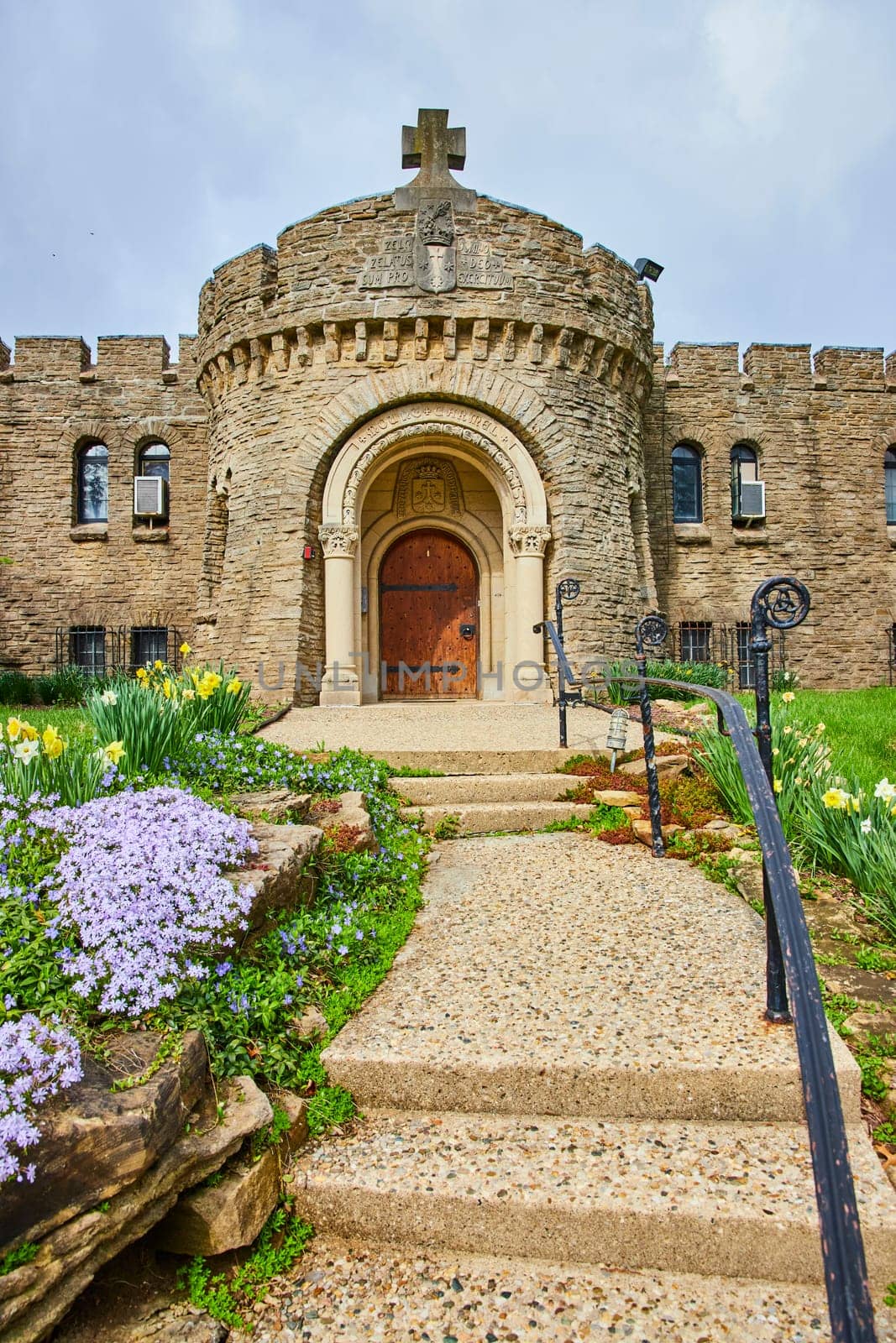 Springtime at Bishop Simon Brute College, showcasing an inviting entrance of a medieval-style stone castle with vibrant floral surrounds.