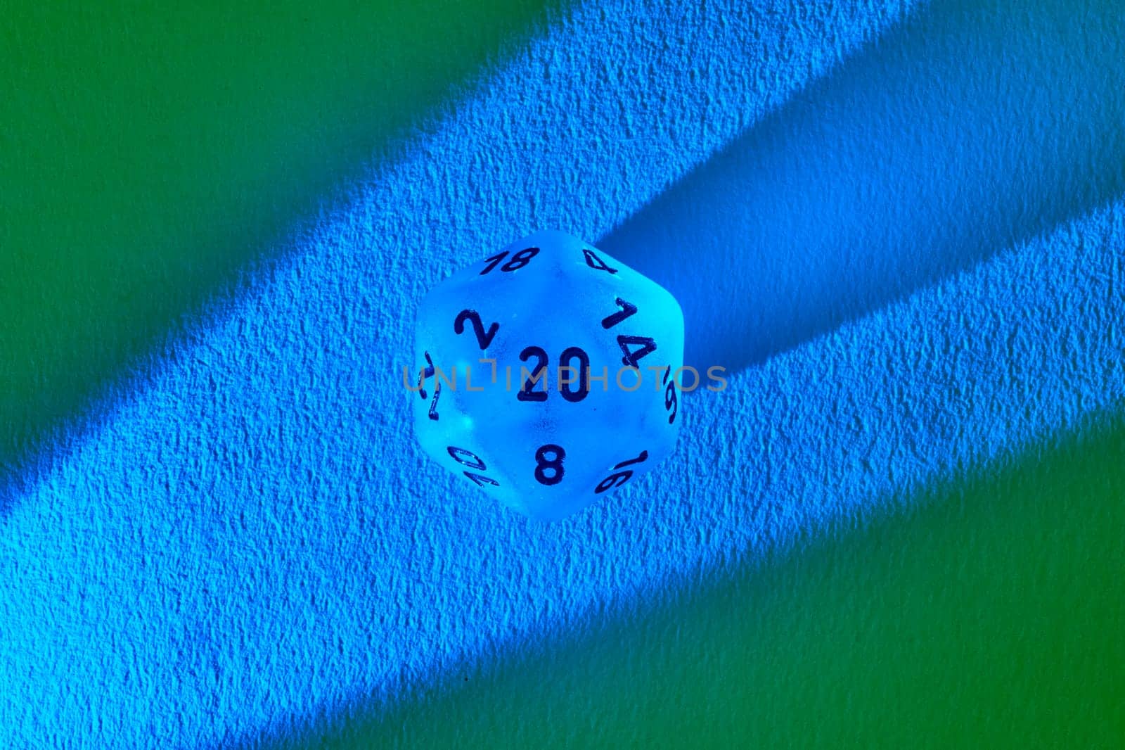 Luminous blue twenty-sided die casting shadow on contrasting green and blue backdrop, symbolizing gaming strategy and the thrill of chance.