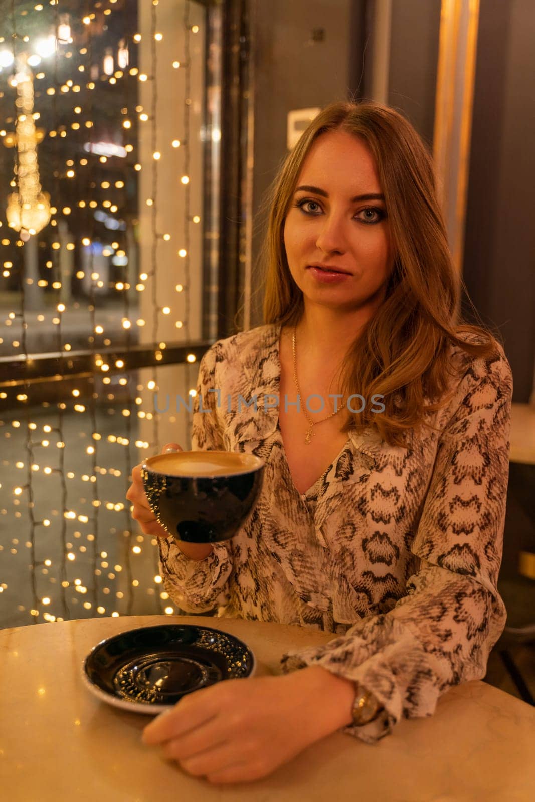 A woman is sitting at a table with a cup of coffee in front of her. She is wearing a snake print dress and she is enjoying her coffee. by Matiunina