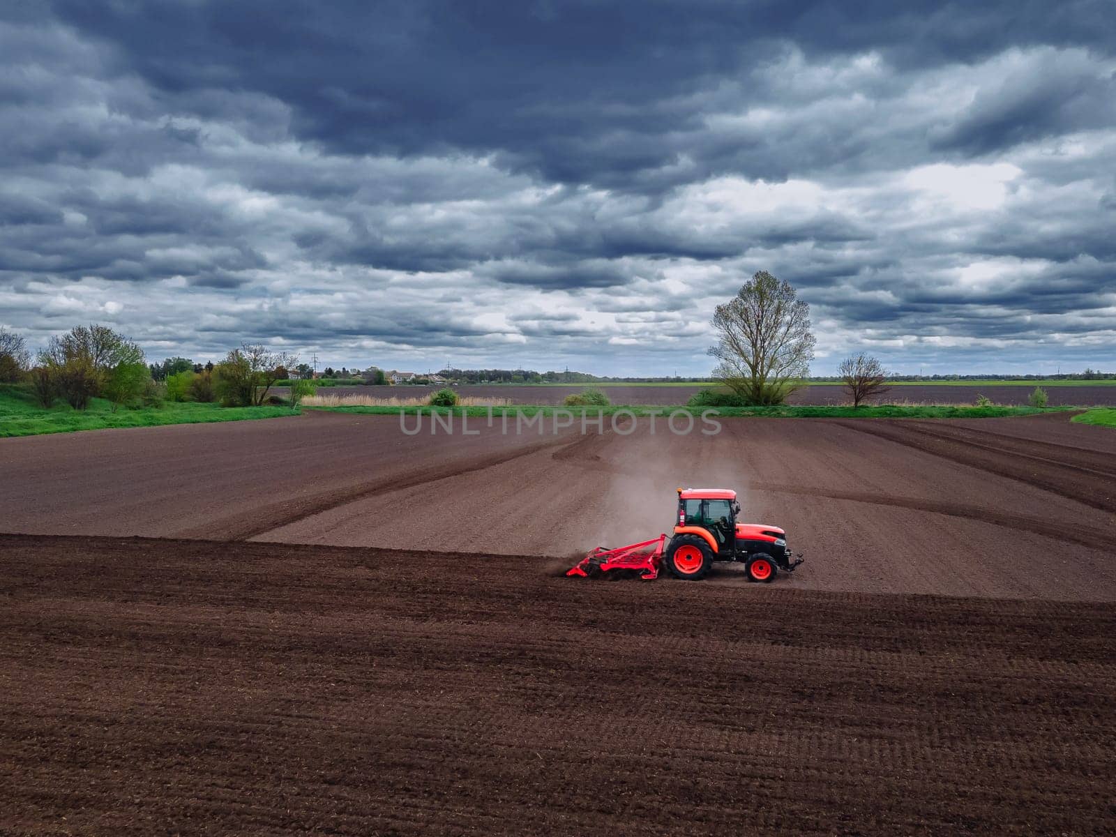 A red tractor working in the field. Agricultural red small tractor in the field plowing, works in the field. Tractor plows the field aerial view. by OnPhotoUa
