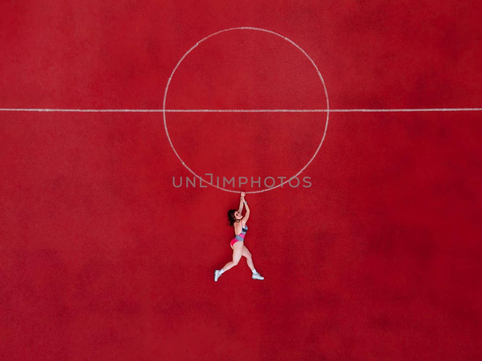 Abstract aerial shot of woman in swimwear hanging holding a circle on basketball field by OnPhotoUa