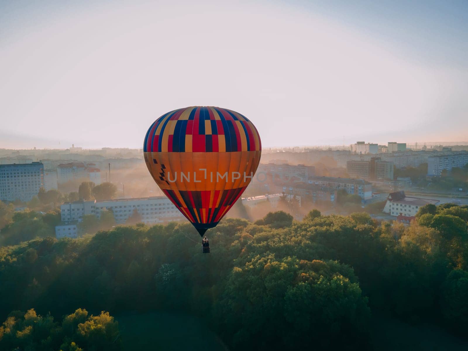 Colorful hot air balloon takes off from green park in small european city at summer sunrise by OnPhotoUa