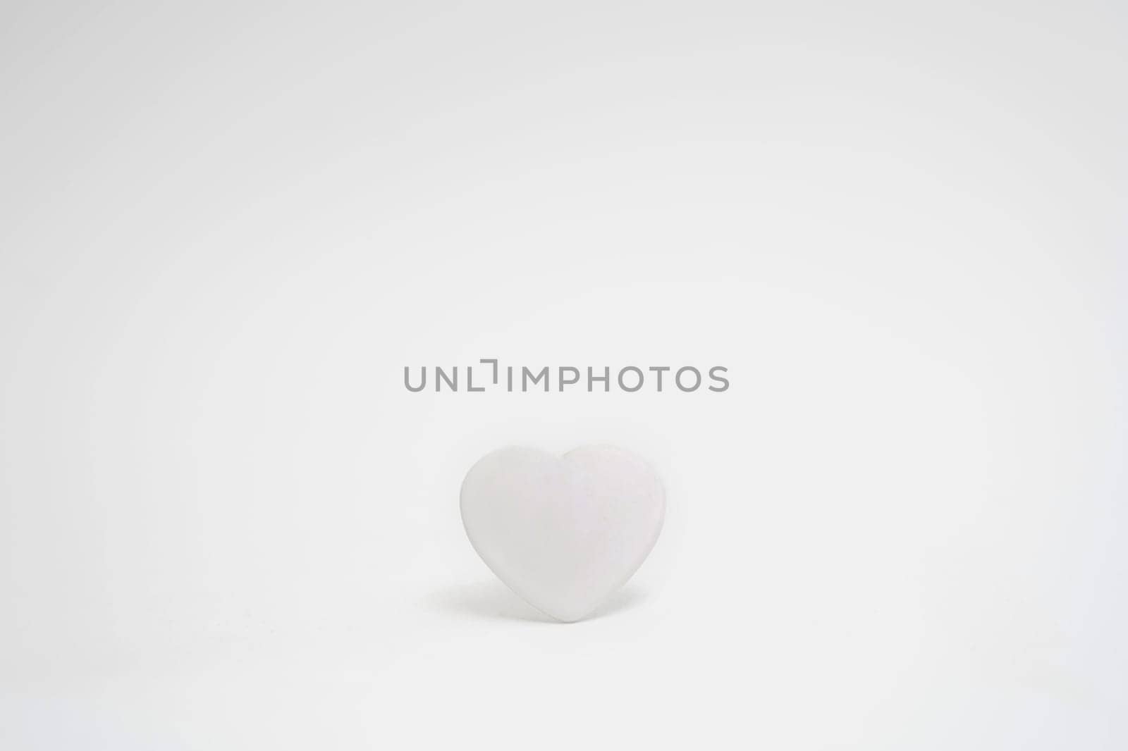 White heart on a white background in the center of the frame. Minimalism. Copy space. Concept of Valentine's Day or wedding romantic theme. Minimalistic high key photo.