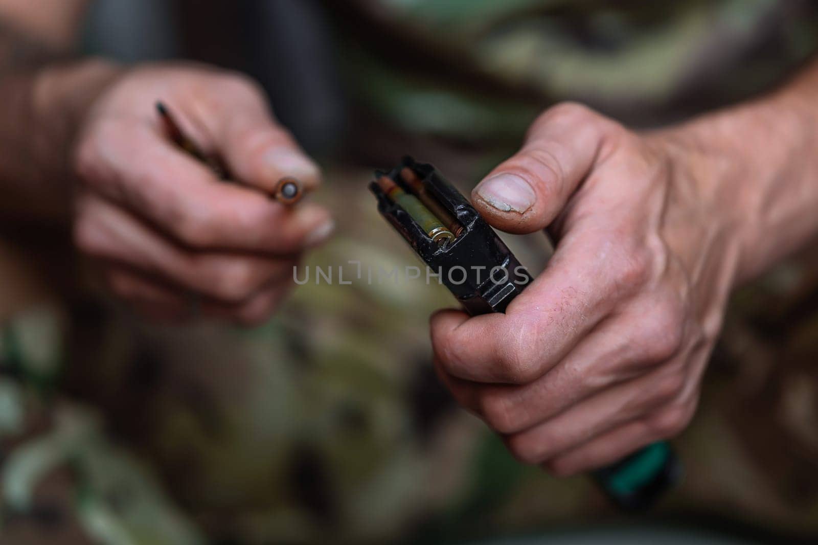 Close-up shot of hands of Ukrainian military man loads the assault rifle magazine with cartridges by OnPhotoUa
