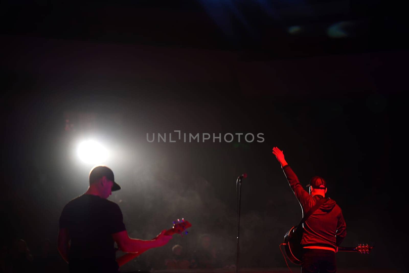 Rock band vocalist silhouette with the guitar singing to microphone with the hands raised up in red lights on the concert