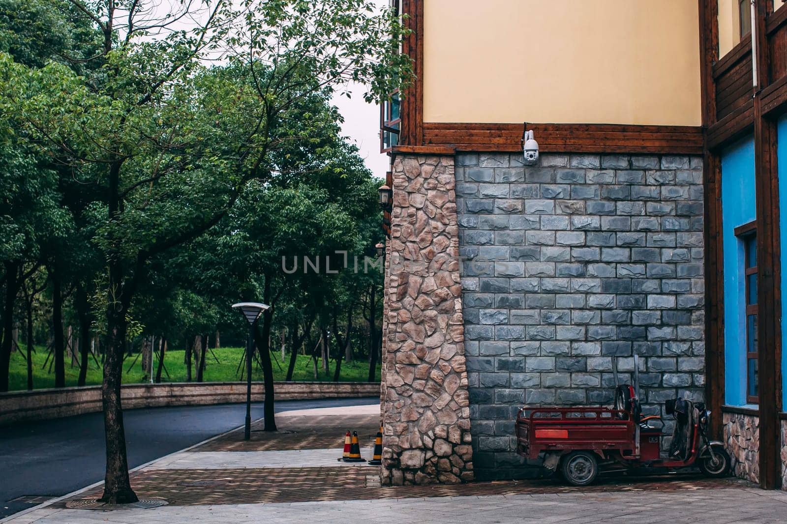 Brick wall of building in chinese park. Asphalt road, motorbike, trees. by OnPhotoUa