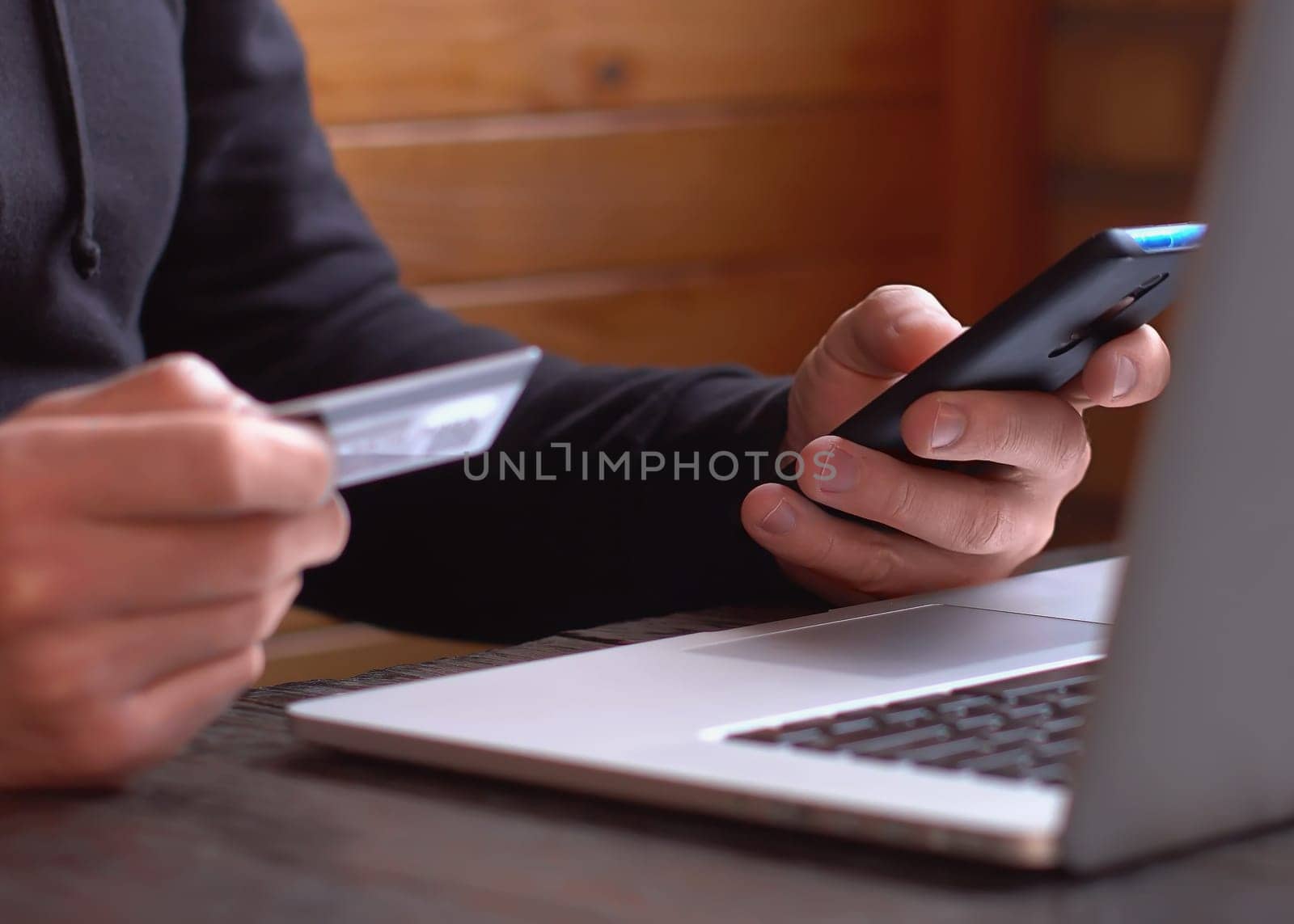 Man in a black hoodie making online payment with credit card and smartphone, online shopping, lifestyle technology. Man enters the bank card number into the smart phone. Closeup. Close up.