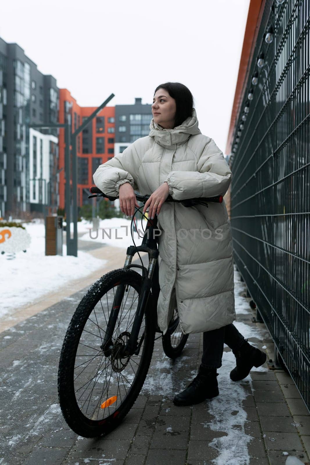A woman is standing next to a bike in a snowy landscape. She is wearing winter clothing and appears to be preparing to ride the bike through the snow-covered terrain.