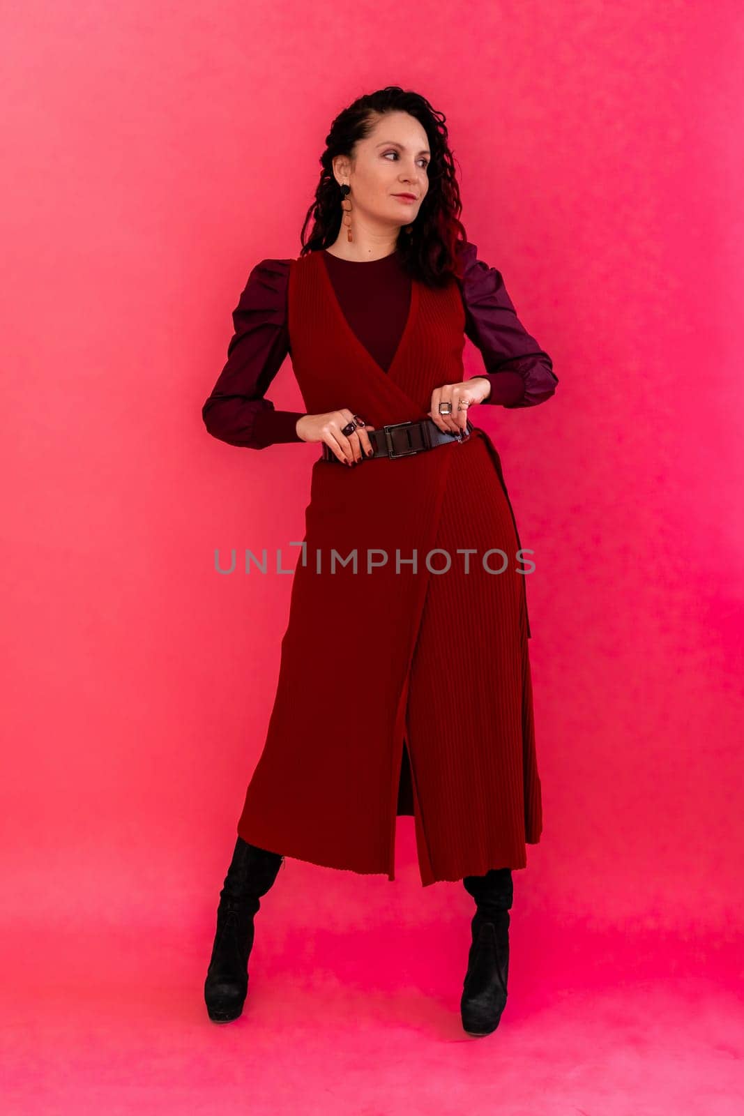 A woman in a red dress poses for the camera. She is wearing black boots and a belt. by Matiunina