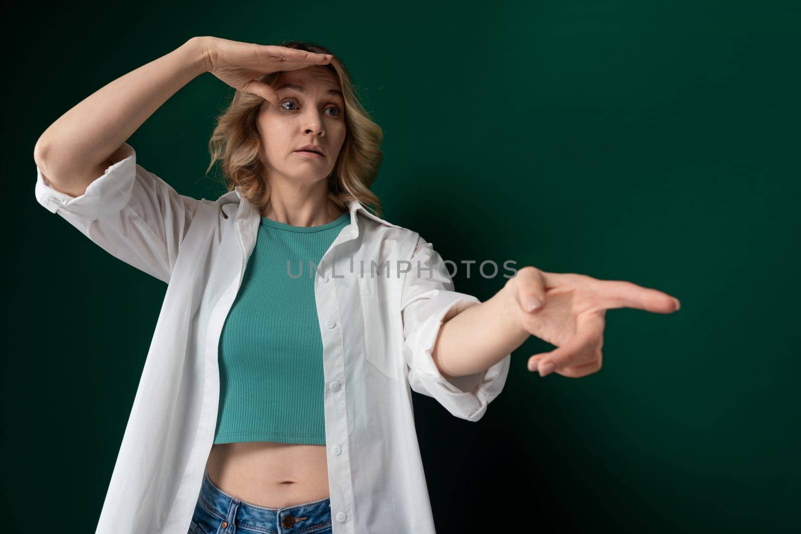 A woman wearing a green shirt is pointing at an unidentified object or subject. Her arm is extended, indicating a specific direction or target. The gesture suggests she is drawing attention to something noteworthy.