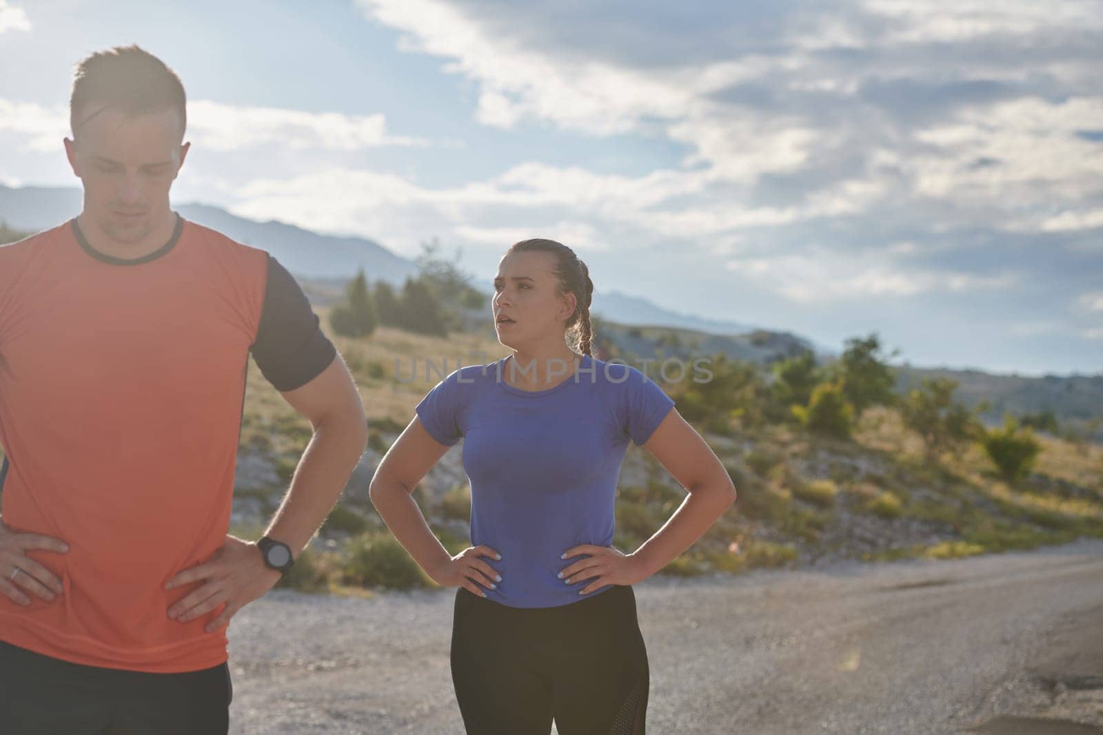 A couple dressed in sportswear runs along a scenic road during an early morning workout, enjoying the fresh air and maintaining a healthy lifestyle.