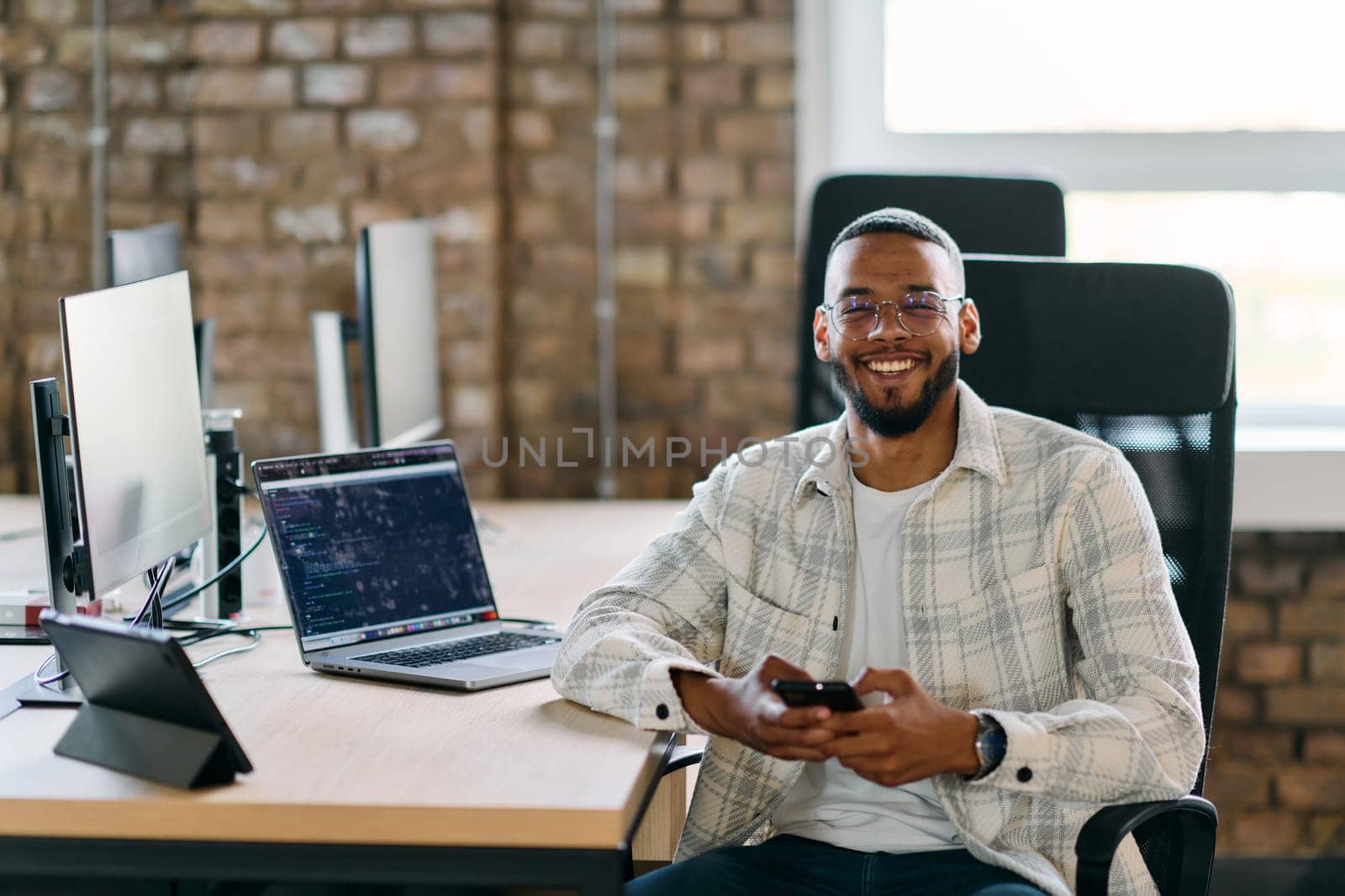 African American entrepreneur takes a break in a modern office, using a smartphone to browse social media, capturing a moment of digital connectivity and relaxation amidst his business endeavors. by dotshock