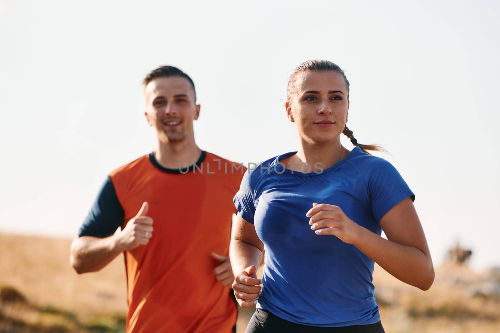 A couple dressed in sportswear runs along a scenic road during an early morning workout, enjoying the fresh air and maintaining a healthy lifestyle.