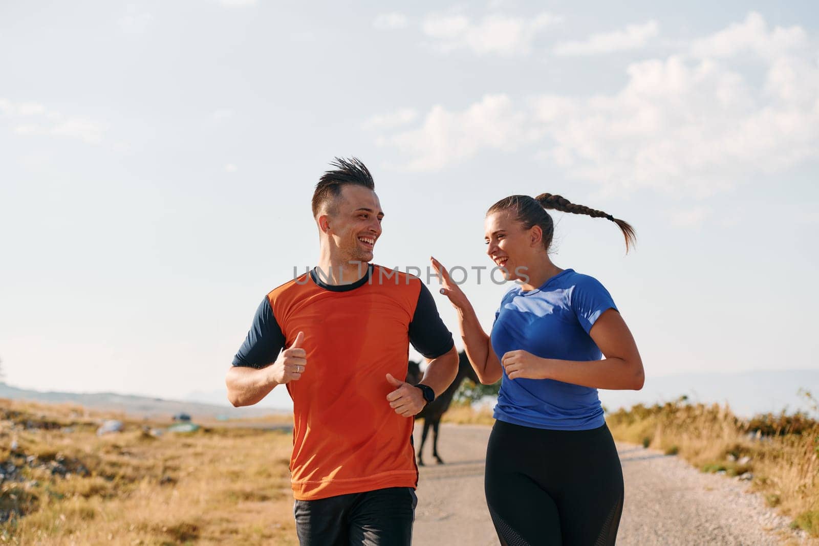 A couple dressed in sportswear runs along a scenic road during an early morning workout, enjoying the fresh air and maintaining a healthy lifestyle by dotshock