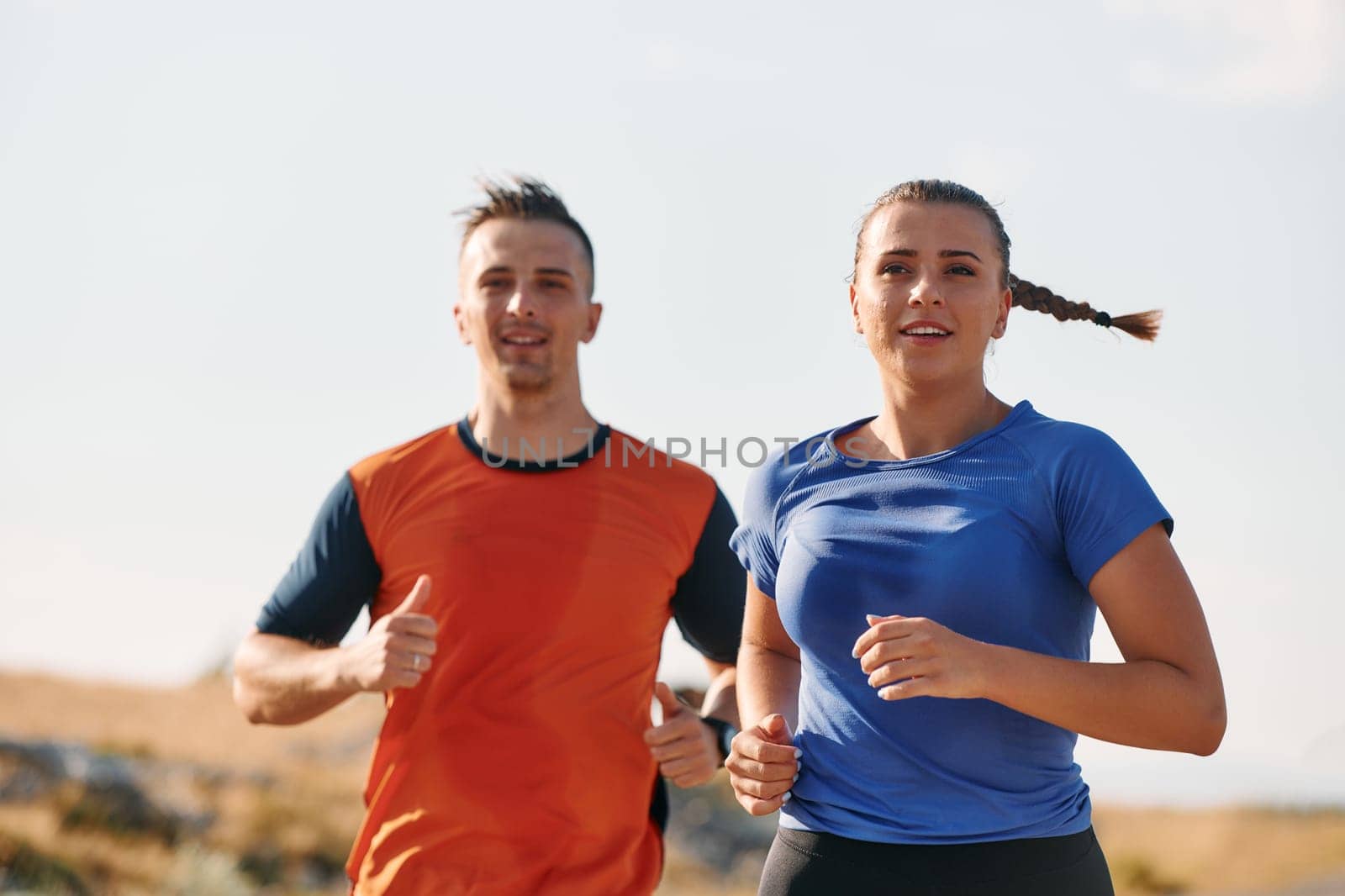 A couple dressed in sportswear runs along a scenic road during an early morning workout, enjoying the fresh air and maintaining a healthy lifestyle by dotshock