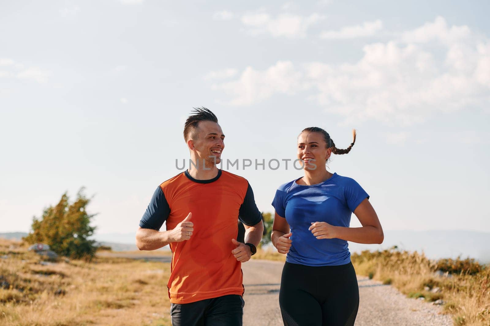 A couple dressed in sportswear runs along a scenic road during an early morning workout, enjoying the fresh air and maintaining a healthy lifestyle by dotshock