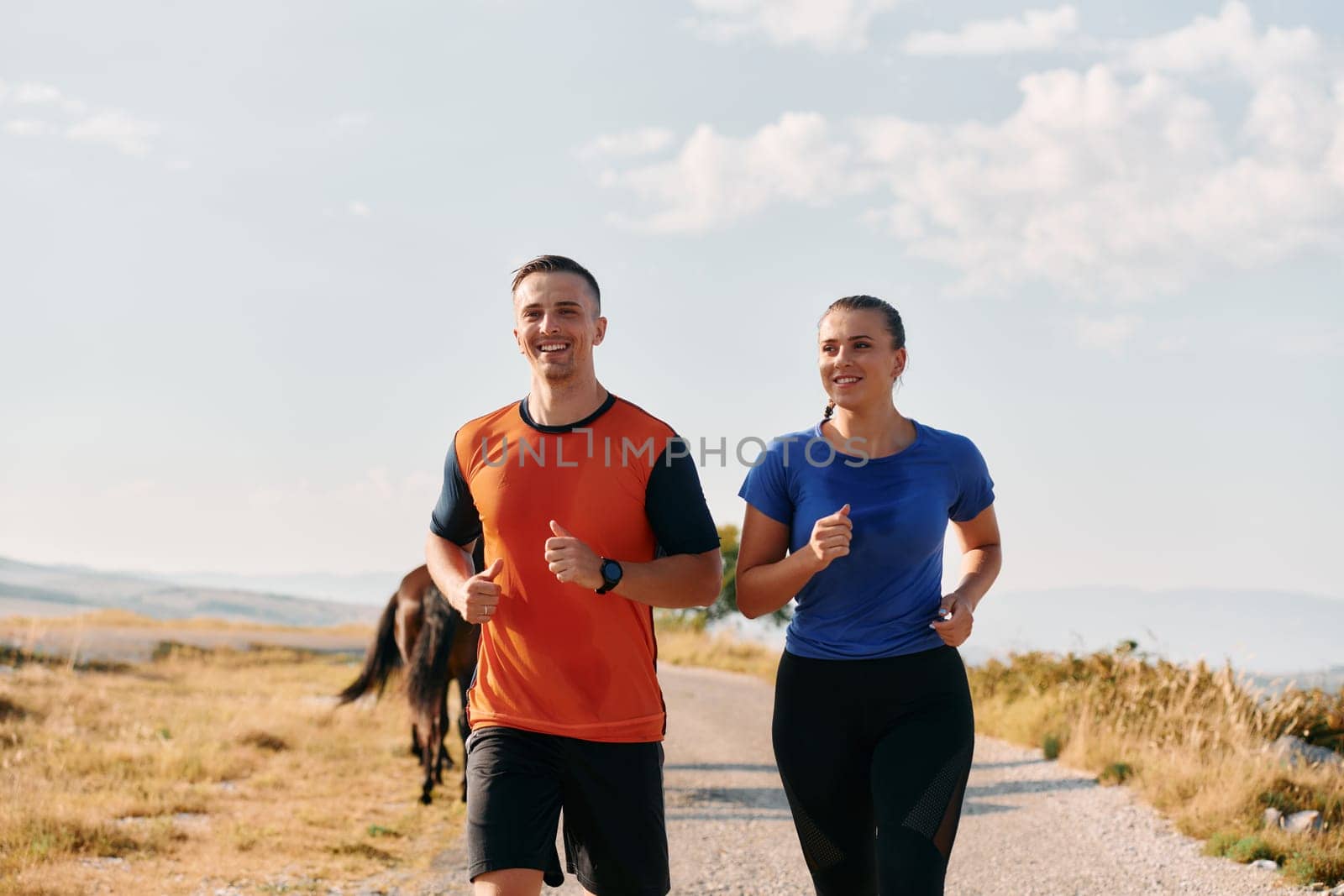 A couple dressed in sportswear runs along a scenic road during an early morning workout, enjoying the fresh air and maintaining a healthy lifestyle by dotshock