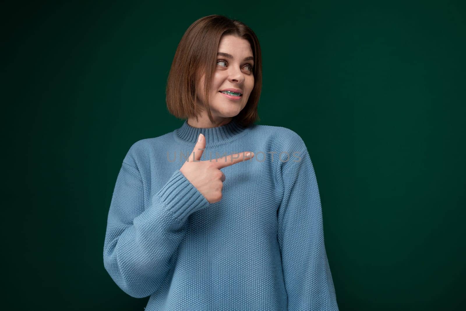 A woman wearing a blue sweater is pointing at an unseen object or direction. She appears focused and engaged in the action of pointing with her arm extended.
