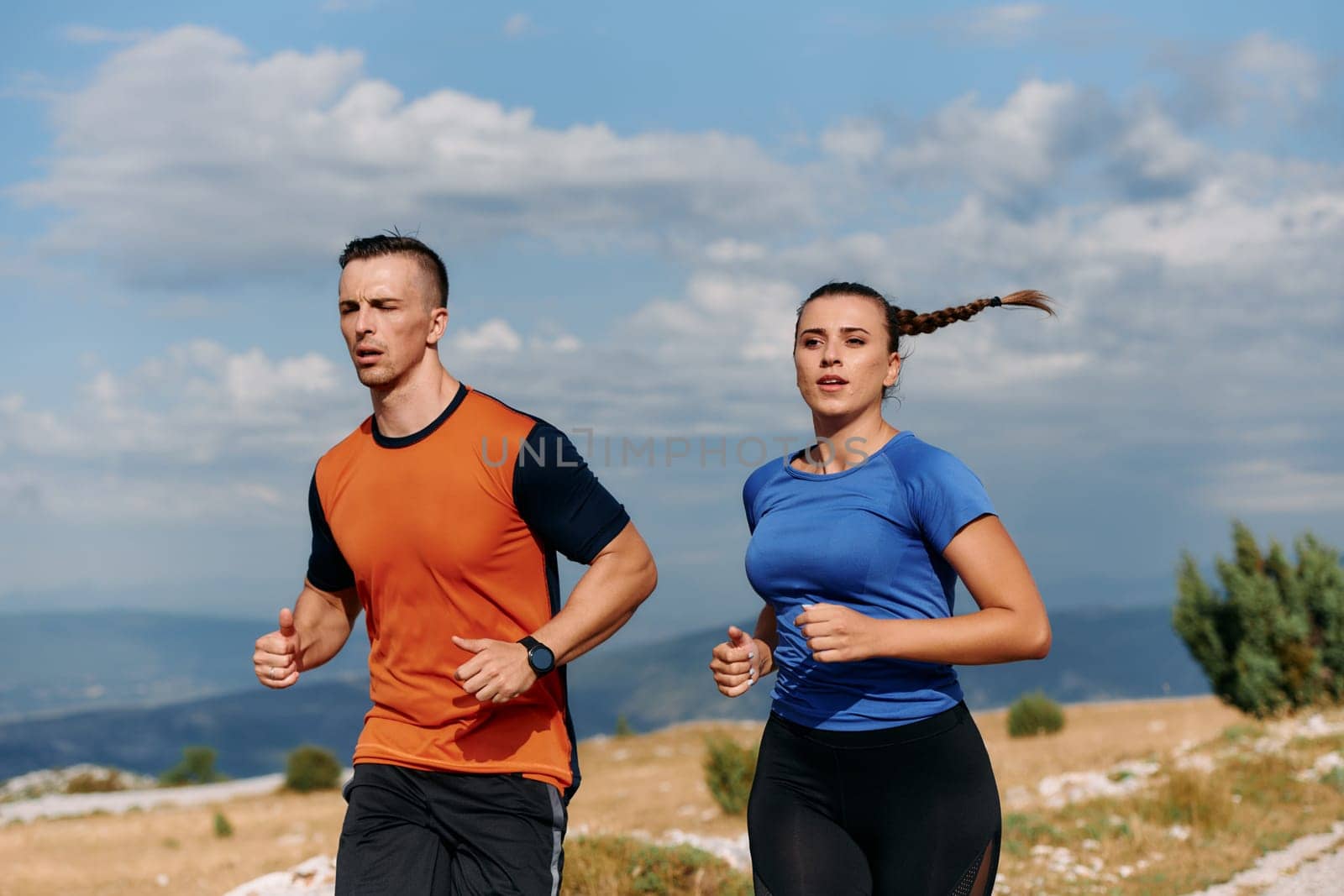 A couple dressed in sportswear runs along a scenic road during an early morning workout, enjoying the fresh air and maintaining a healthy lifestyle.