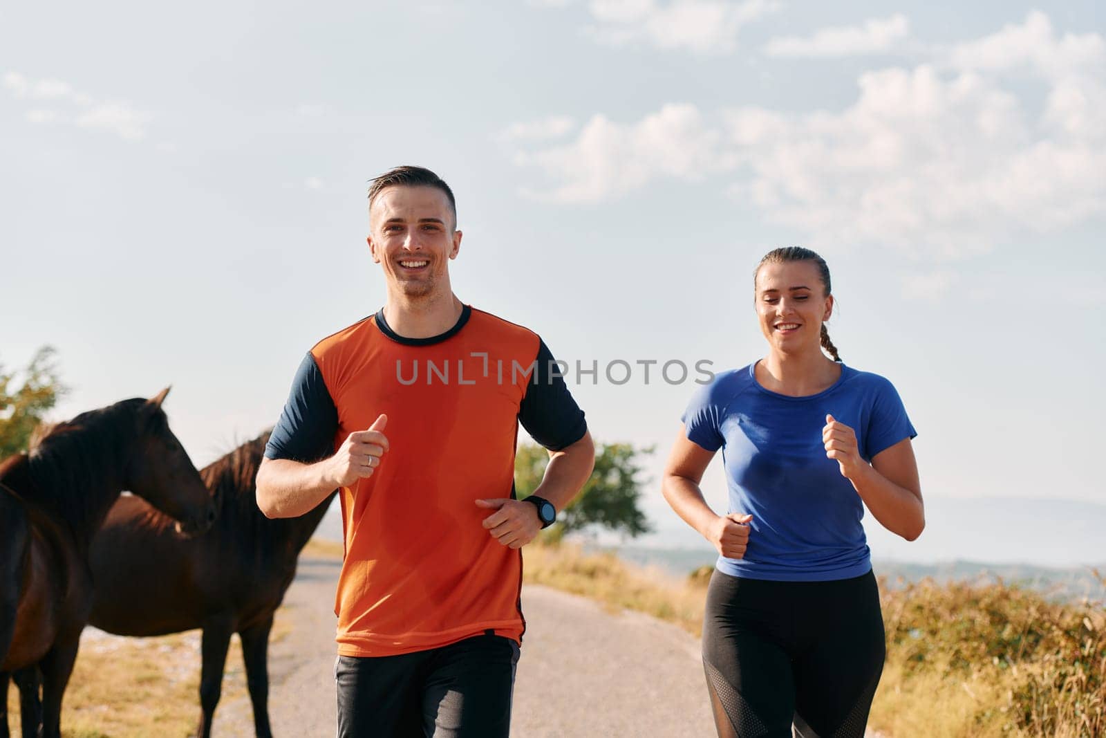 A couple dressed in sportswear runs along a scenic road during an early morning workout, enjoying the fresh air and maintaining a healthy lifestyle by dotshock