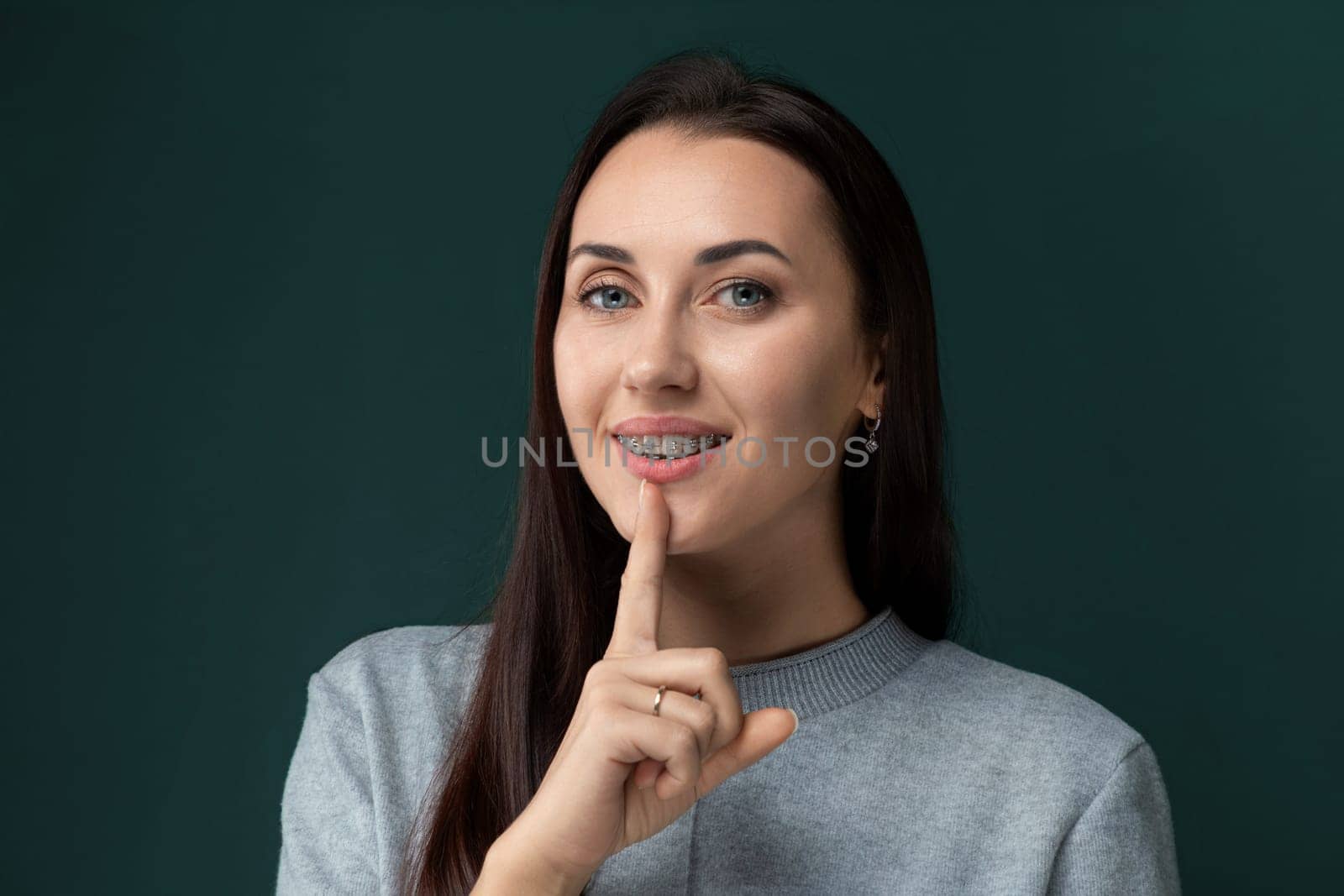 A woman holding a finger to her lips, signaling for silence or quietness. She appears to be asking for discretion or secrecy in a gesture commonly associated with keeping a secret or maintaining silence.