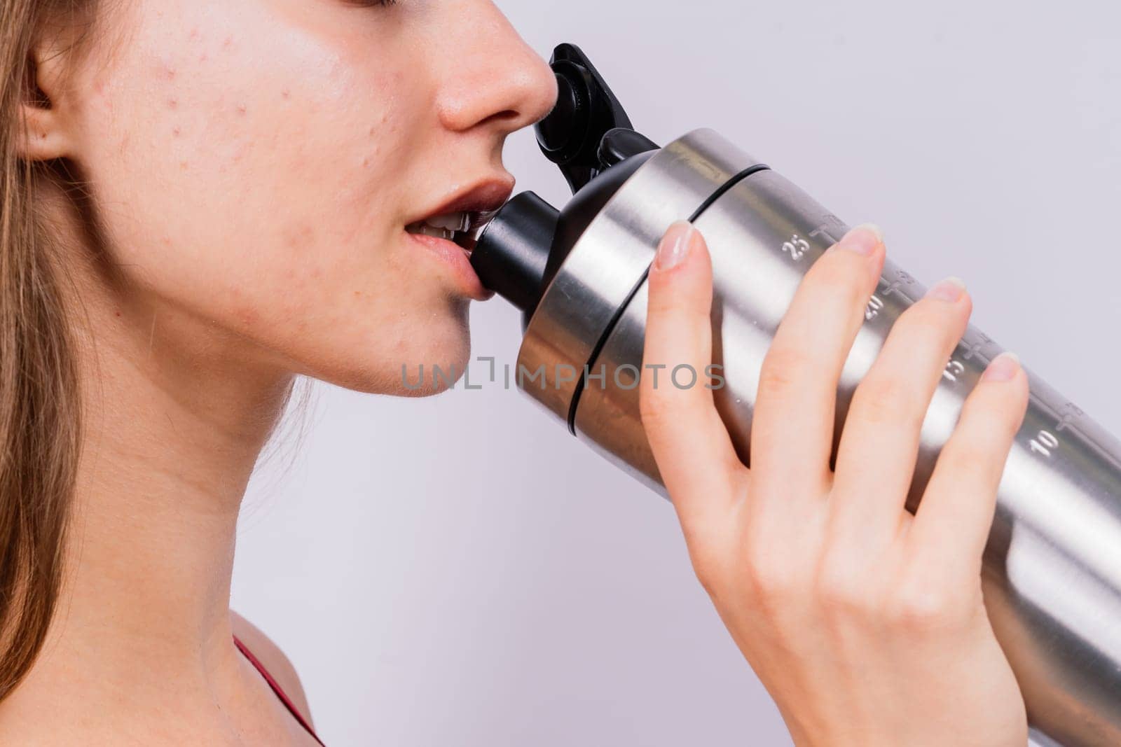Closeup side view of sportive female after training who drinking fresh water from sport bottle by Zelenin