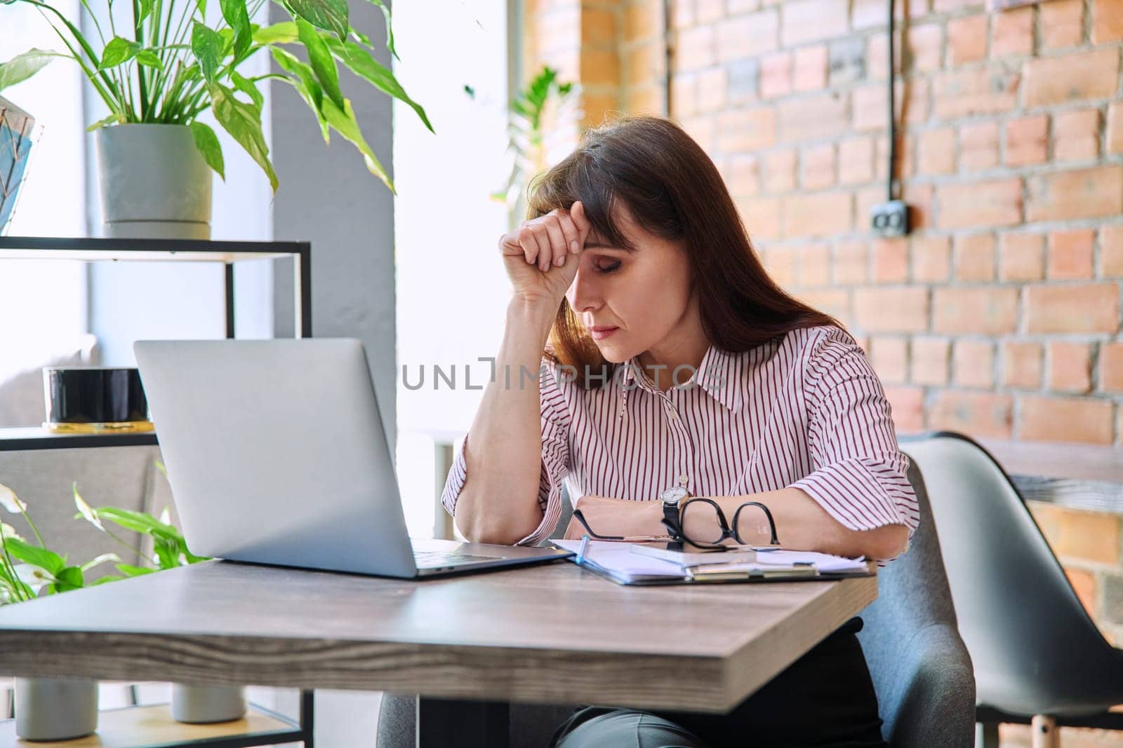 Mature tired worried tense woman at workplace experiencing stress headache by VH-studio