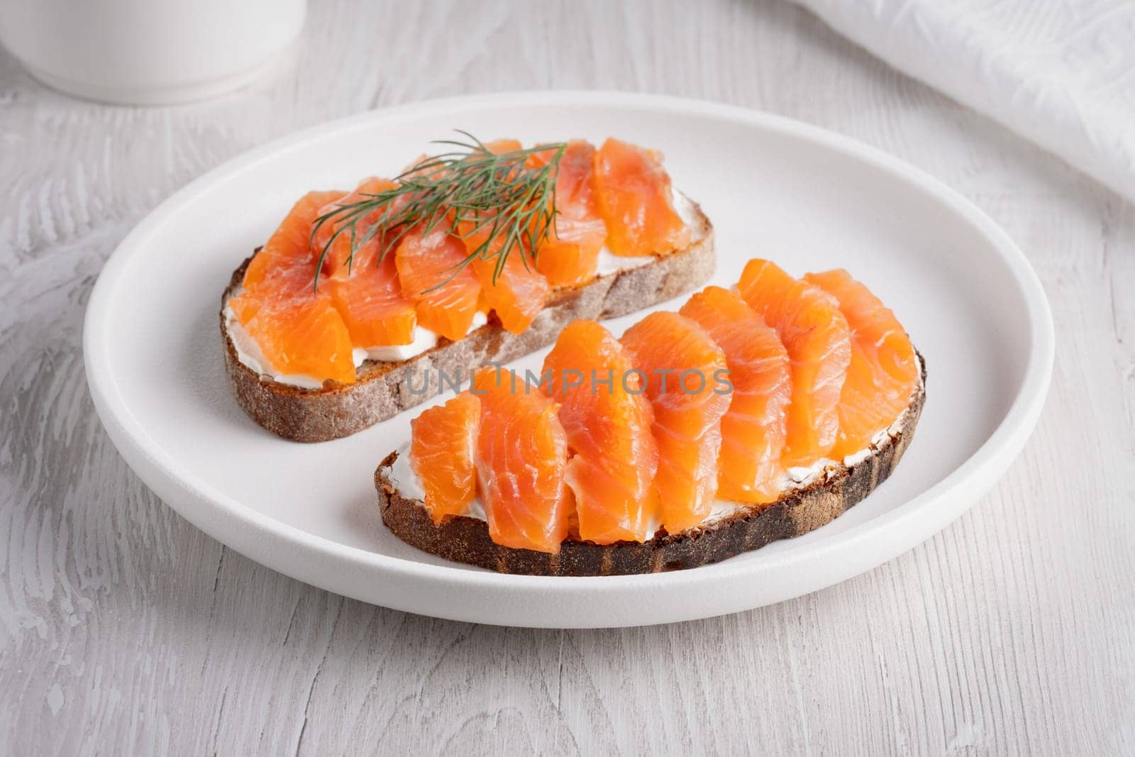Rye sandwich with salmon and cream cheese on white wooden table by NataliPopova