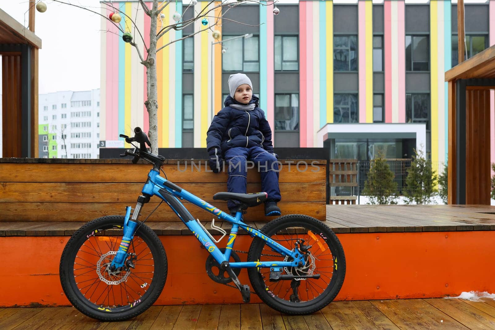 A European boy dressed in a winter jacket gets off his bike by TRMK