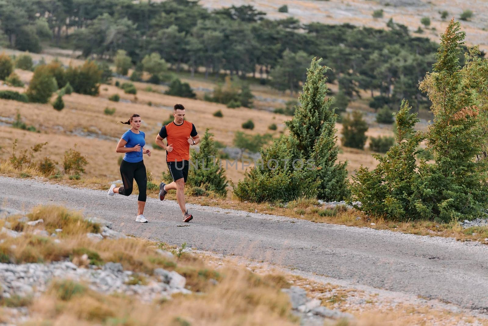 A couple dressed in sportswear runs along a scenic road during an early morning workout, enjoying the fresh air and maintaining a healthy lifestyle.