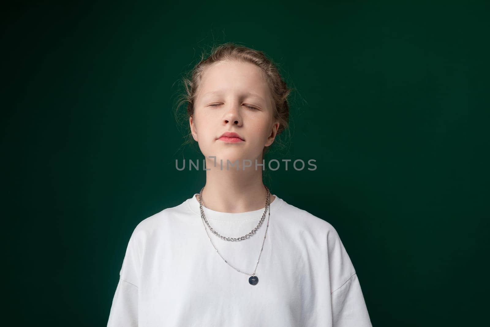 A woman with her eyes closed is standing in front of a solid green background. She appears calm and contemplative, with a serene expression on her face.