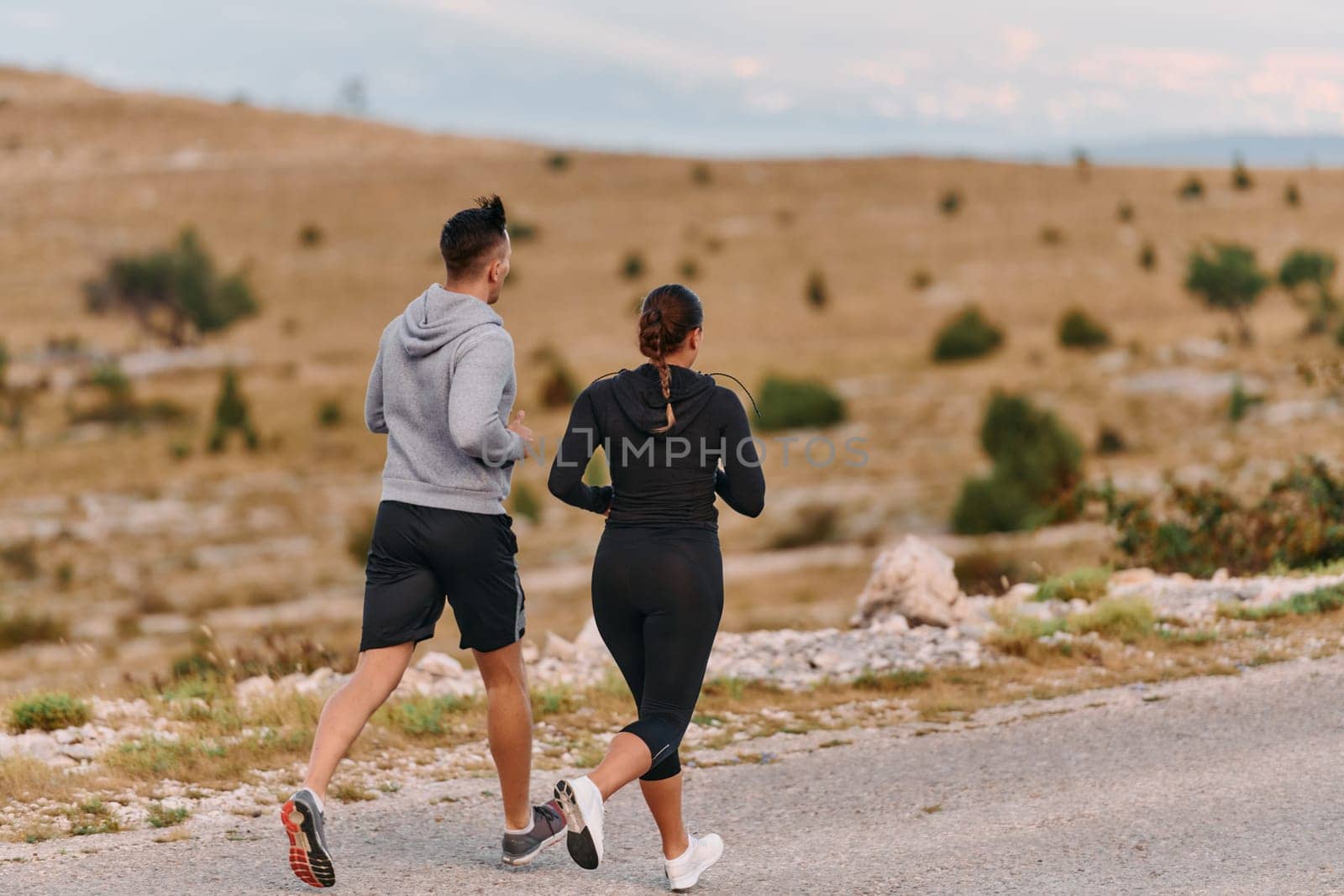 A couple dressed in sportswear runs along a scenic road during an early morning workout, enjoying the fresh air and maintaining a healthy lifestyle by dotshock