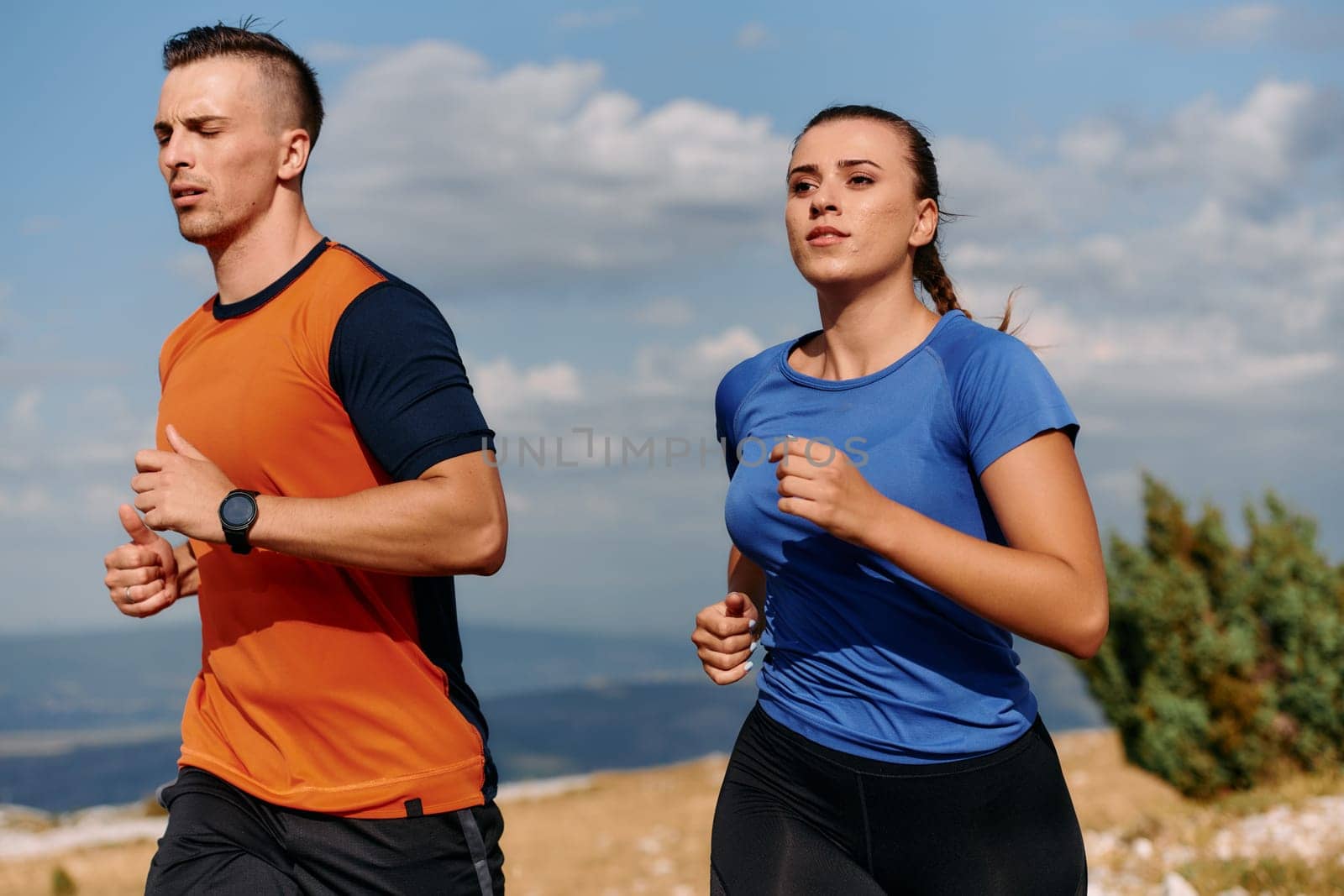 A couple dressed in sportswear runs along a scenic road during an early morning workout, enjoying the fresh air and maintaining a healthy lifestyle.