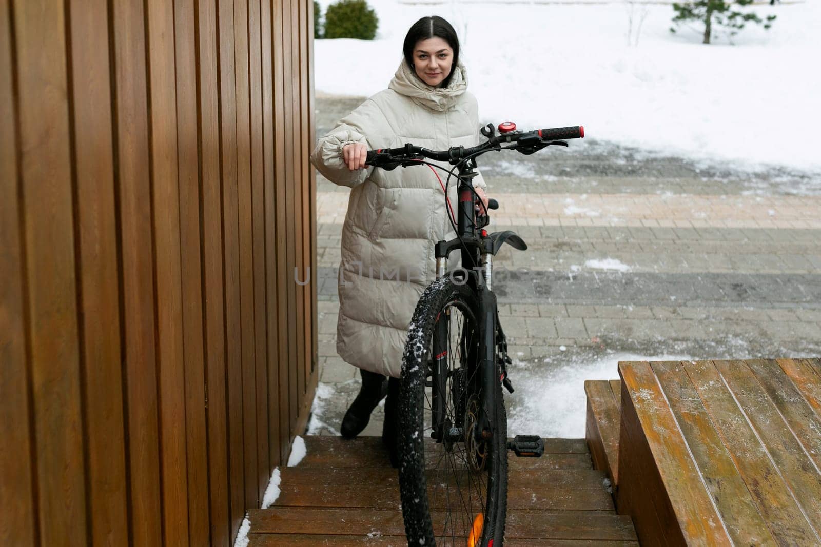 A woman is standing next to a bicycle in a snowy landscape. She appears to be dressed warmly for the cold weather, with snow covering the ground around her.