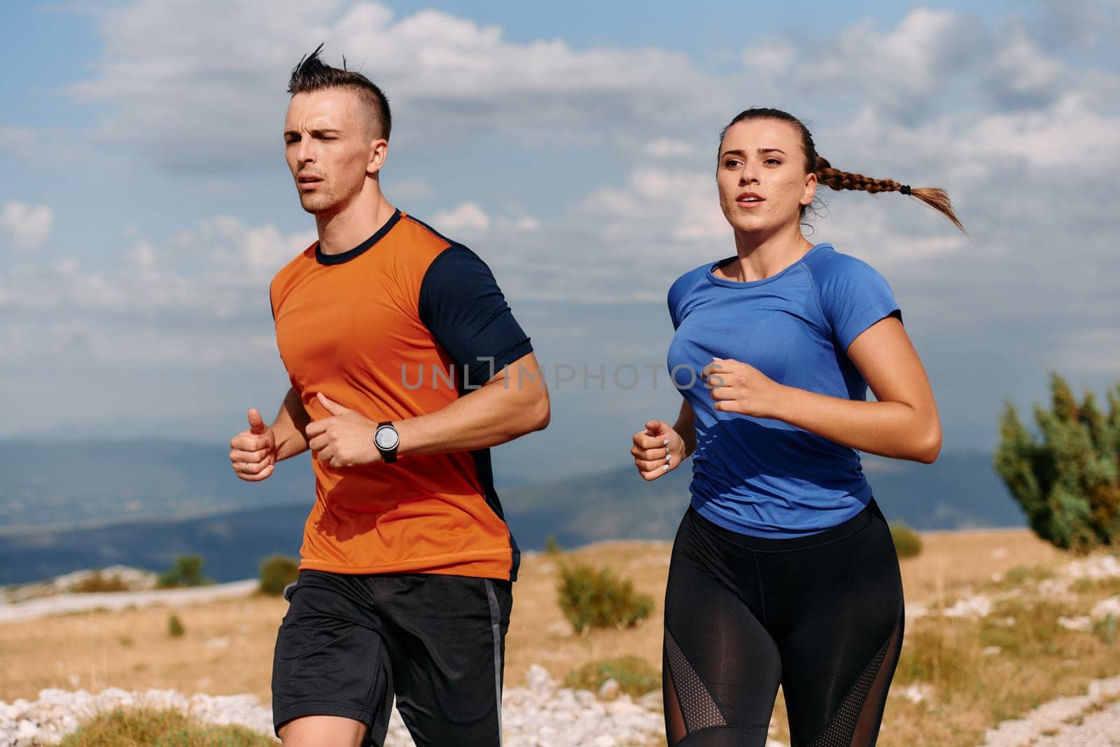 A couple dressed in sportswear runs along a scenic road during an early morning workout, enjoying the fresh air and maintaining a healthy lifestyle by dotshock