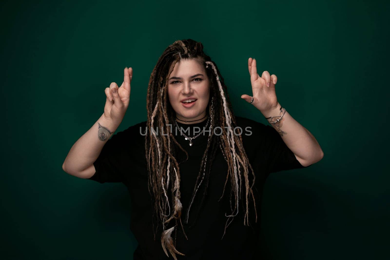 A woman with dreadlocks stands confidently in front of a bright green background. Her hair is styled in thick, textured twists that fall past her shoulders. The womans expression is focused and determined.