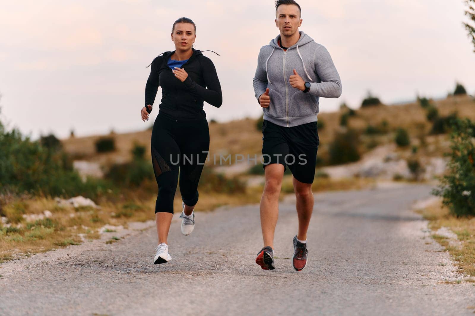 A couple dressed in sportswear runs along a scenic road during an early morning workout, enjoying the fresh air and maintaining a healthy lifestyle by dotshock