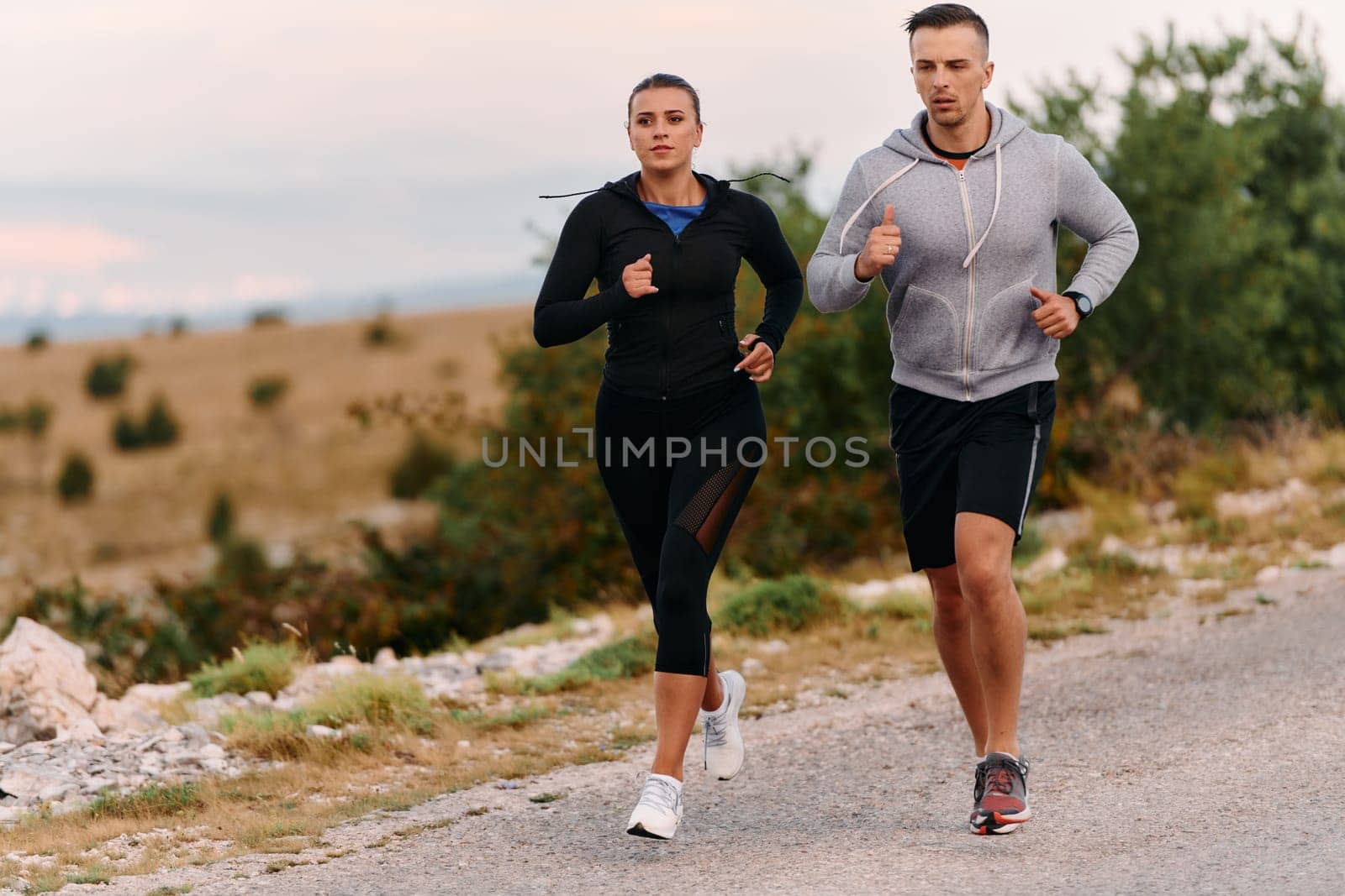 A couple dressed in sportswear runs along a scenic road during an early morning workout, enjoying the fresh air and maintaining a healthy lifestyle.