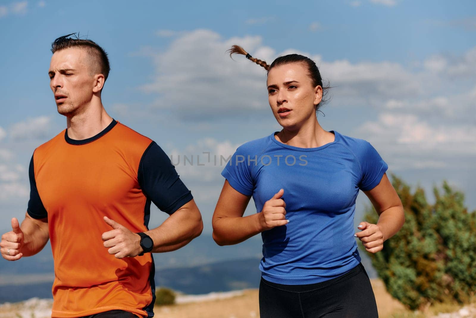 A couple dressed in sportswear runs along a scenic road during an early morning workout, enjoying the fresh air and maintaining a healthy lifestyle.