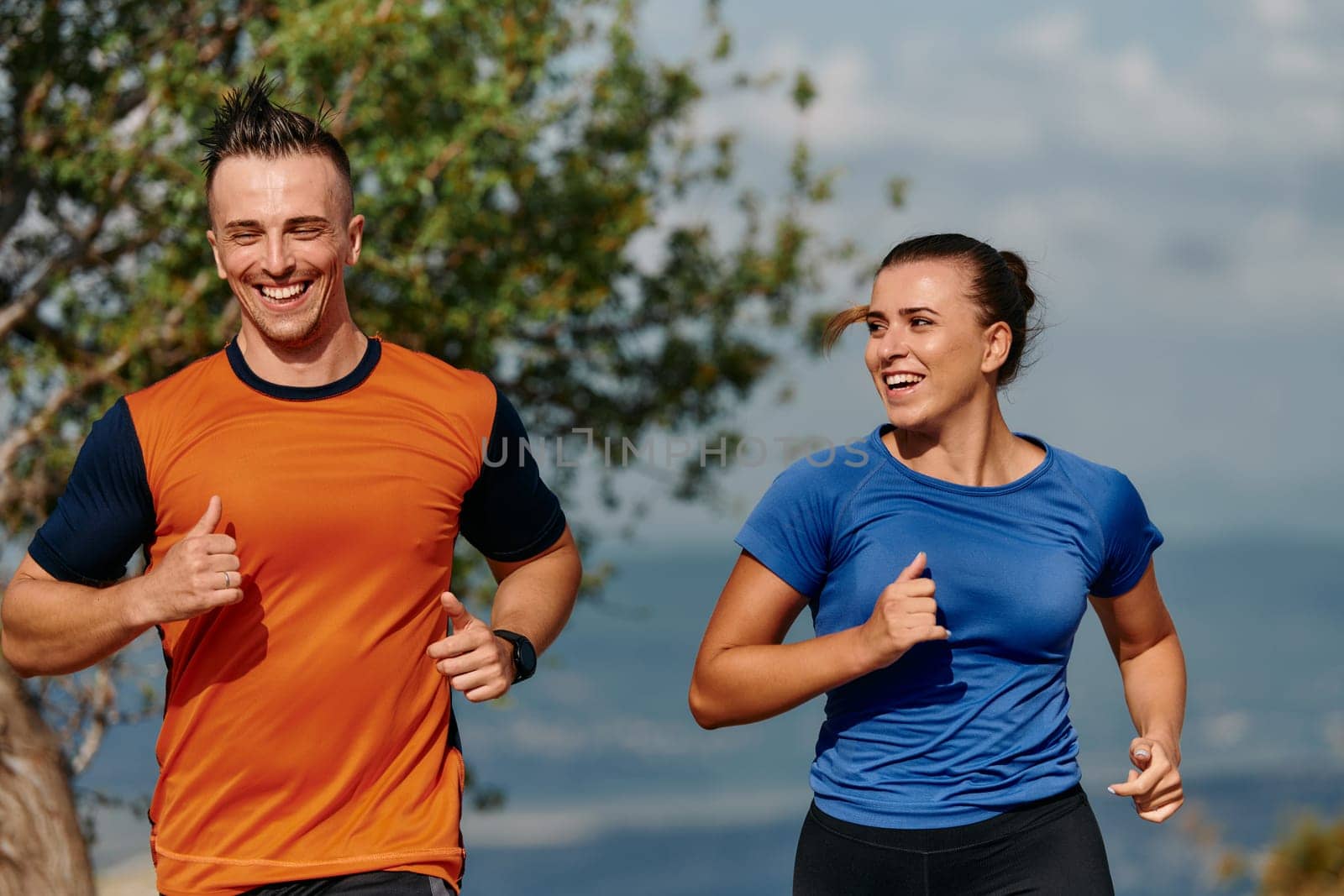 A couple dressed in sportswear runs along a scenic road during an early morning workout, enjoying the fresh air and maintaining a healthy lifestyle.