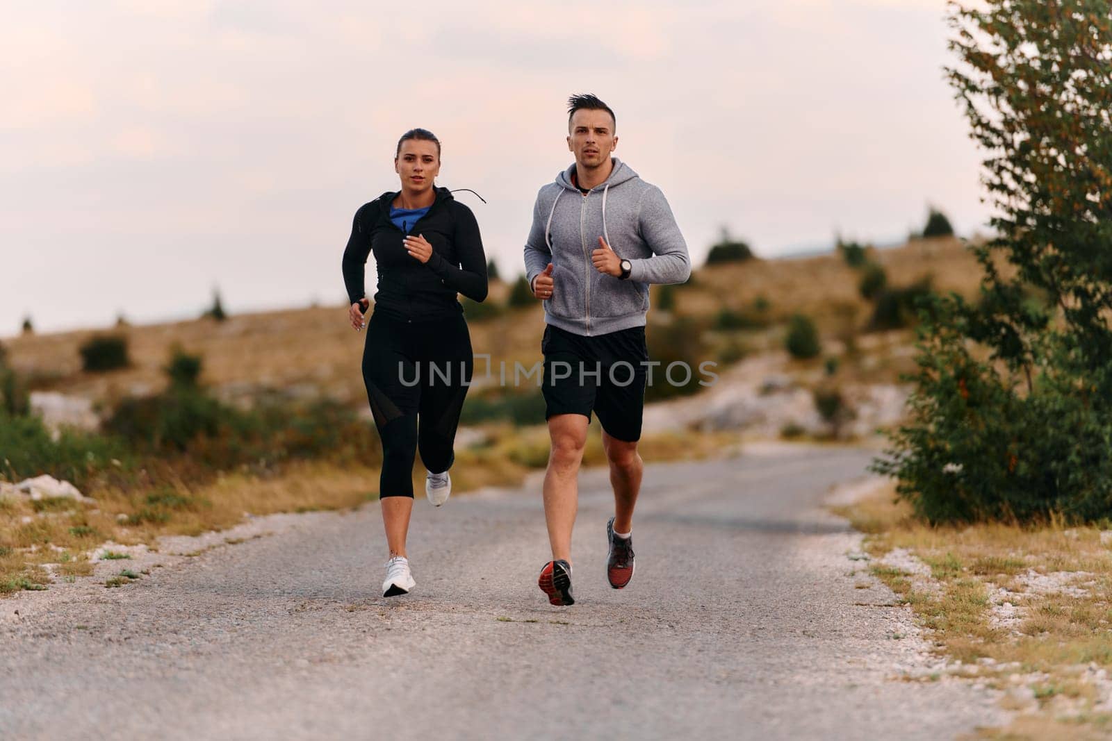 A couple dressed in sportswear runs along a scenic road during an early morning workout, enjoying the fresh air and maintaining a healthy lifestyle.