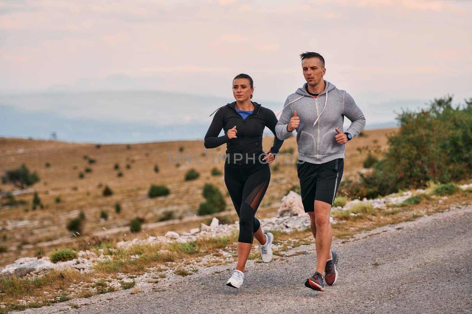 A couple dressed in sportswear runs along a scenic road during an early morning workout, enjoying the fresh air and maintaining a healthy lifestyle by dotshock