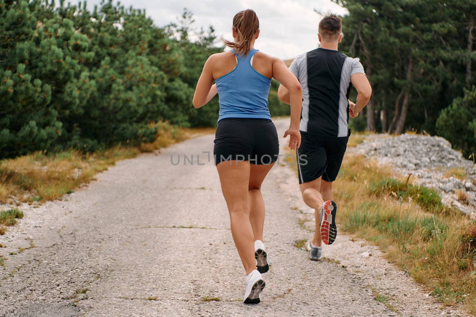 A couple dressed in sportswear runs along a scenic road during an early morning workout, enjoying the fresh air and maintaining a healthy lifestyle by dotshock