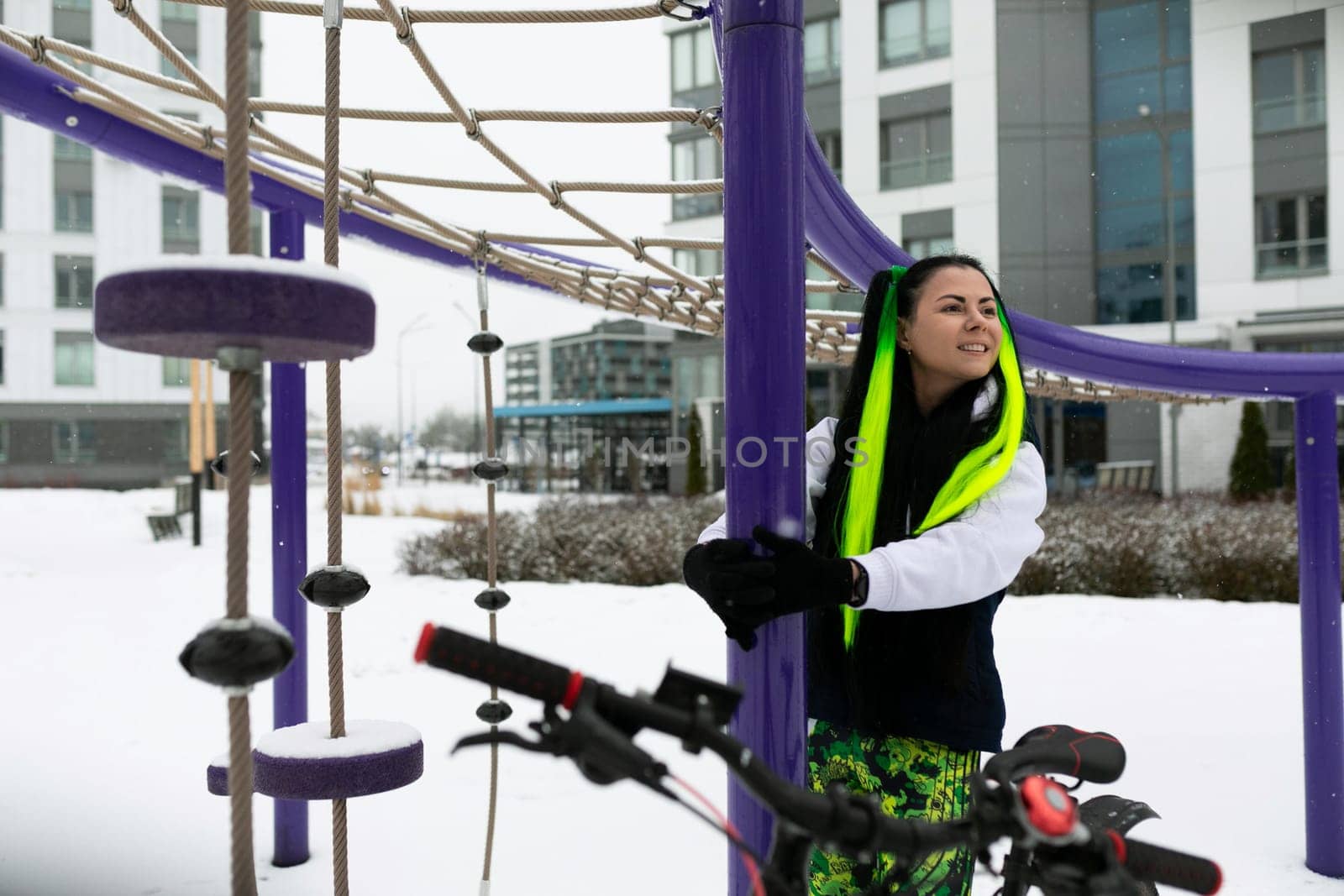 A woman stands next to a bicycle in a snowy outdoor setting. She is dressed warmly, with snowflakes visible around her.