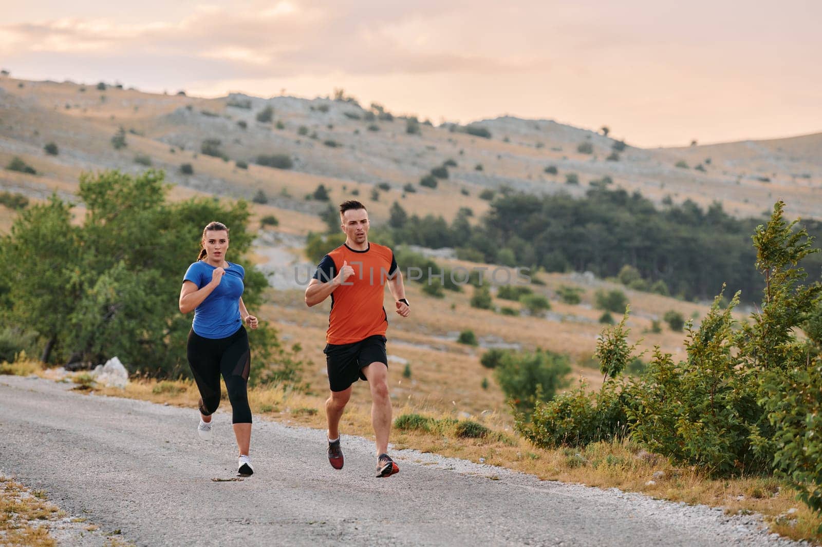 A couple dressed in sportswear runs along a scenic road during an early morning workout, enjoying the fresh air and maintaining a healthy lifestyle.