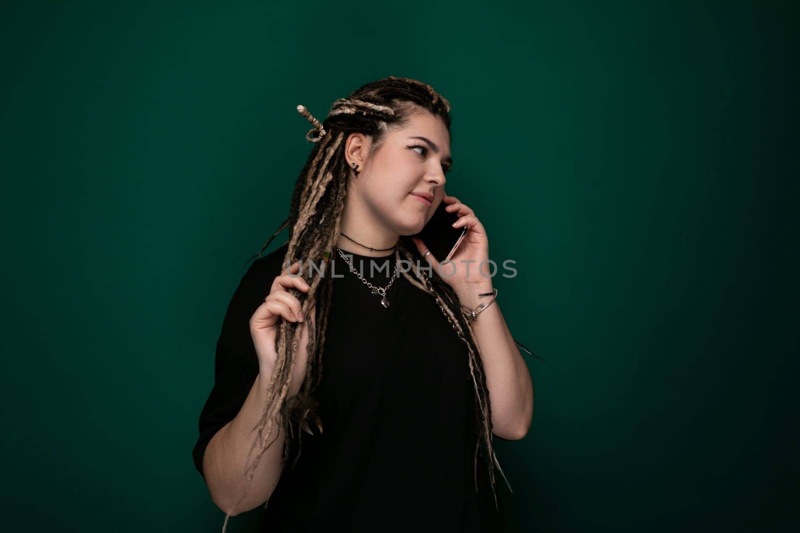 A woman with dreadlocks is engaged in a phone conversation, holding a cell phone to her ear while speaking. Her facial expression suggests she is focused on the call.