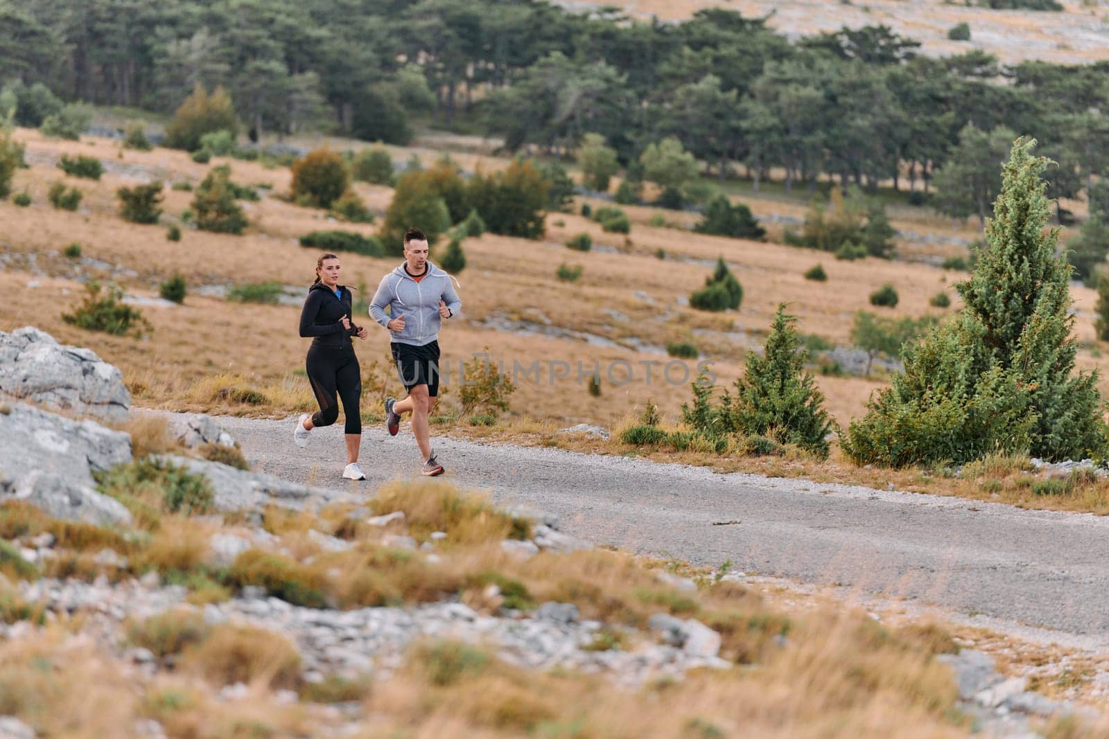 A couple dressed in sportswear runs along a scenic road during an early morning workout, enjoying the fresh air and maintaining a healthy lifestyle by dotshock