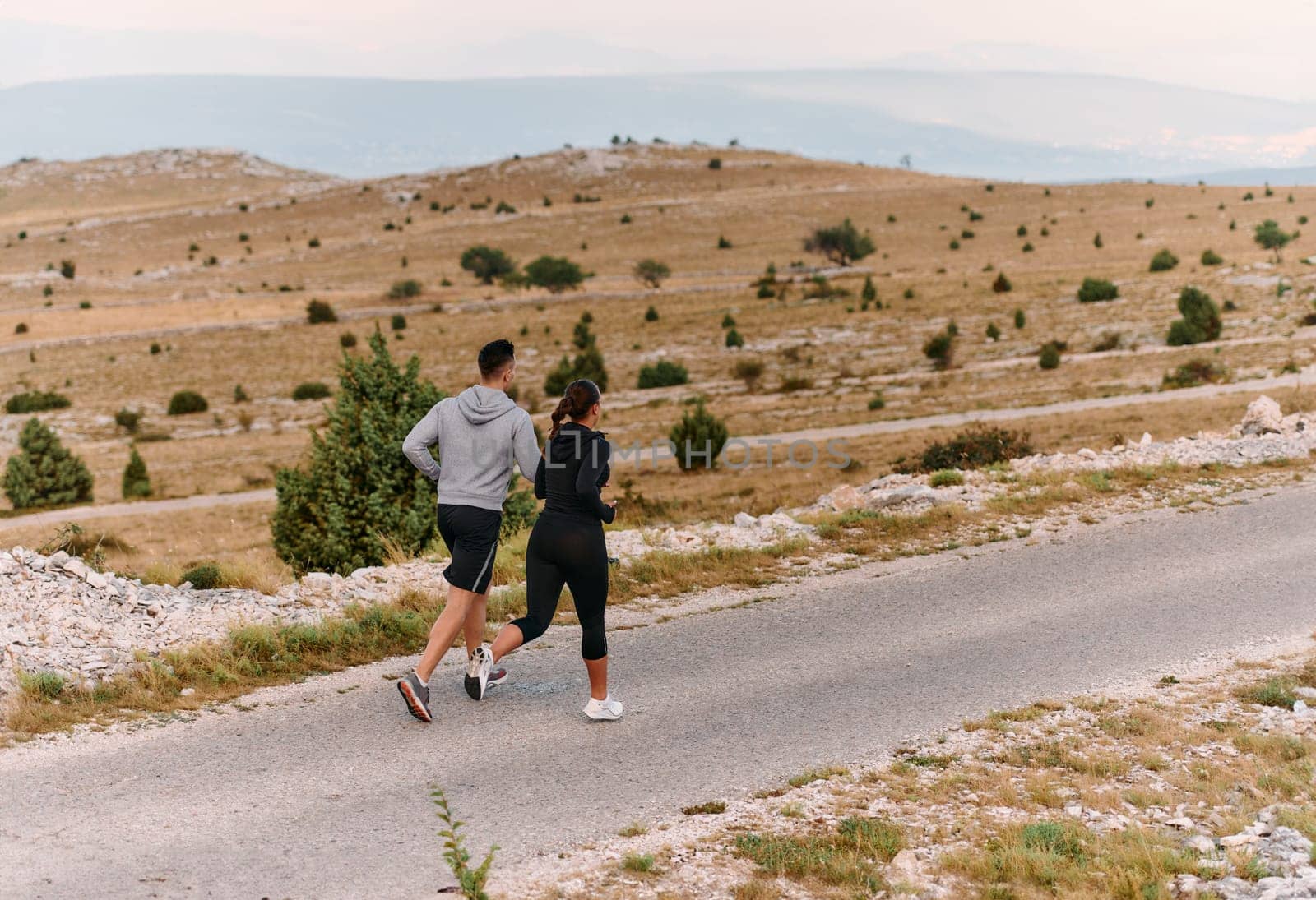 A couple dressed in sportswear runs along a scenic road during an early morning workout, enjoying the fresh air and maintaining a healthy lifestyle by dotshock